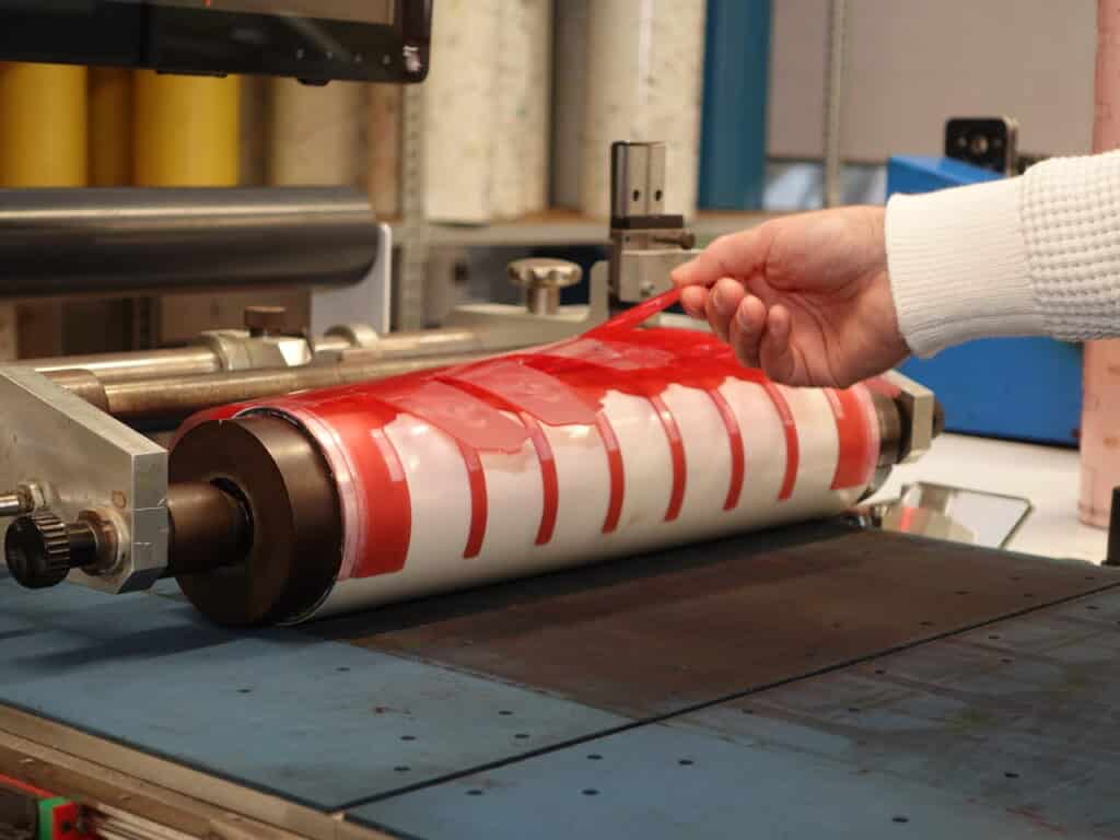Opérateur retirant un film adhésif rouge sur le rouleau d'une machine de lamination